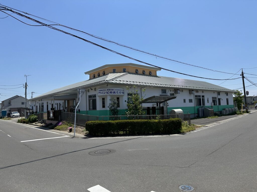 Two-story building with a yellow upper section and metal roof at a street corner, power lines overhead and a tidy green-painted base.
